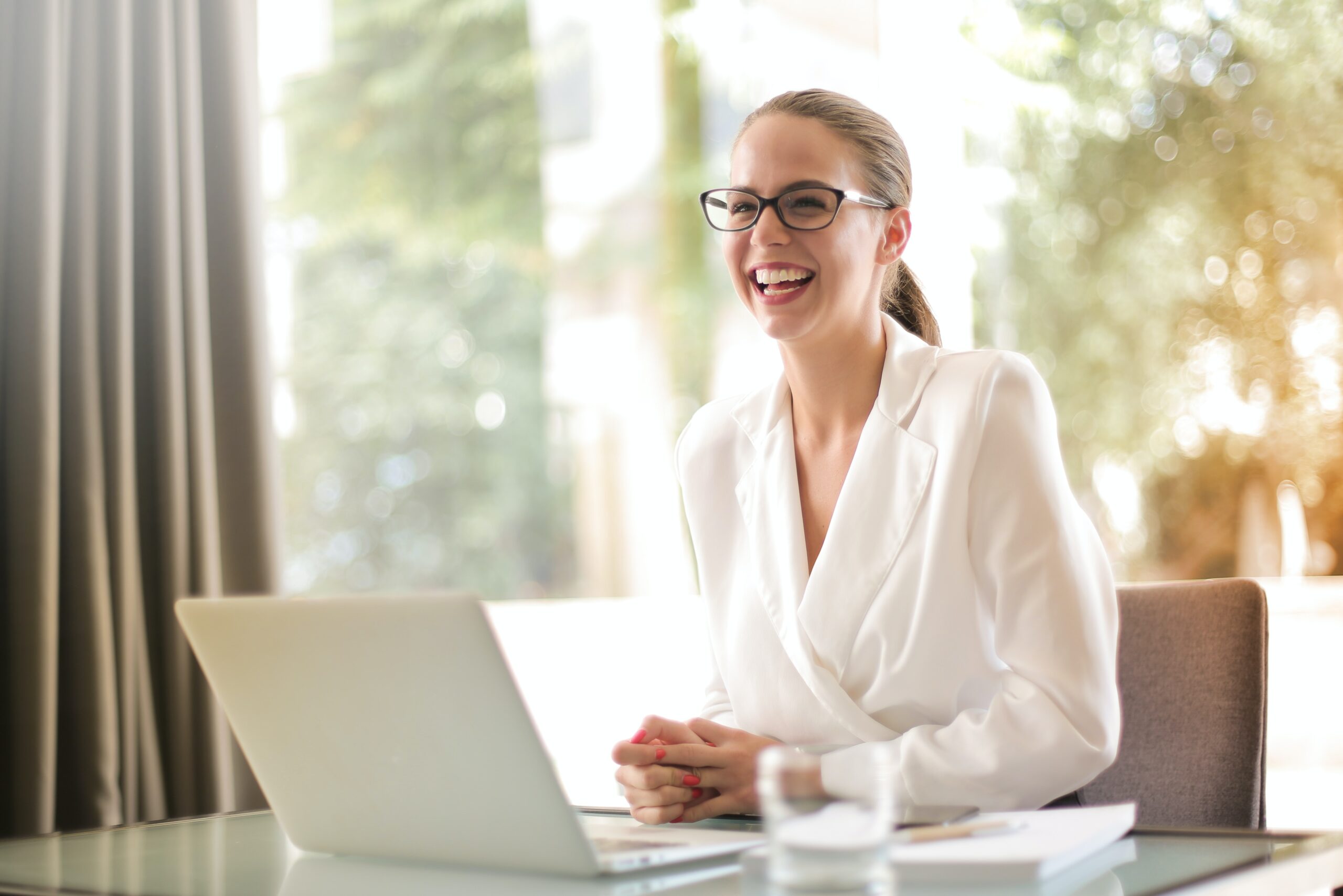 Woman smiling, sat at a desk in front of her laptop