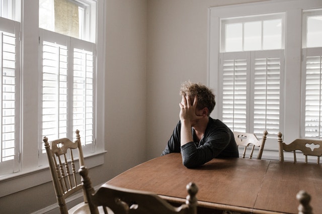 Man at the table, with his hands in his head looking worried and hopeless