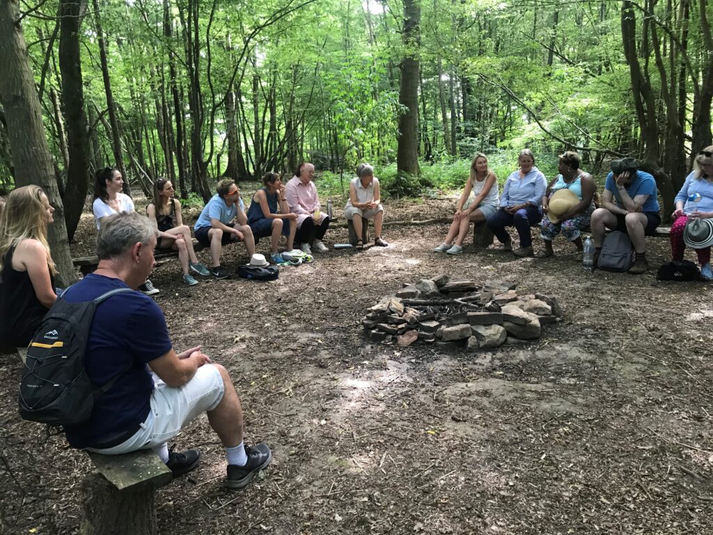 A group of people sitting in circle in a woodland area