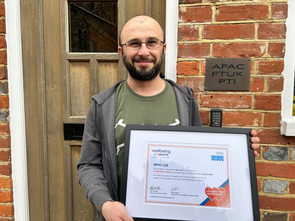 A person holding the Commitment Award certificate in front of their office. 