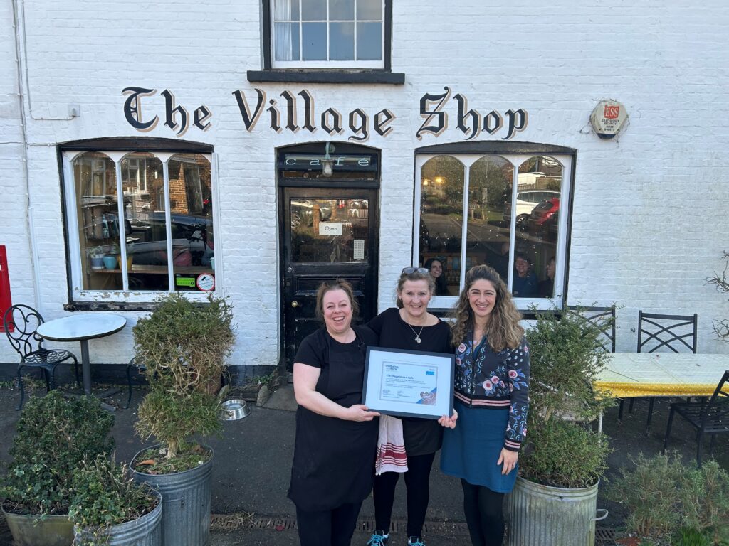 Three women standing outside a cafe holding a framed certificate for Small Business Bronze Award